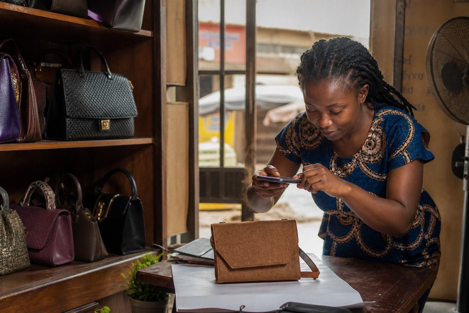 Nigerian small-business owner photographing real products with a smartphone inside a modest shop
